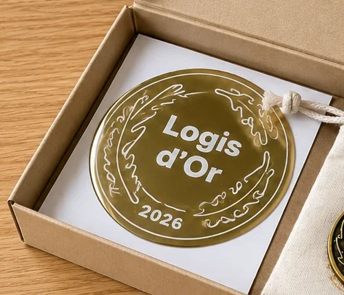 Le macaron Logis d'Or 2026, doré, posé dans son coffret